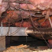 #9 Crawlspace Before - This photo shows numerous damages and hazards, molded and water retaining insulation, hanging electrical wiring, unlevel crawlspace floor, construction debris, and no vapor barrier.